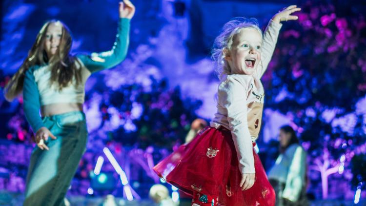 Girl wearing red and cream Christmas outfit dancing in the Med Biome with the Christmas lights behind her