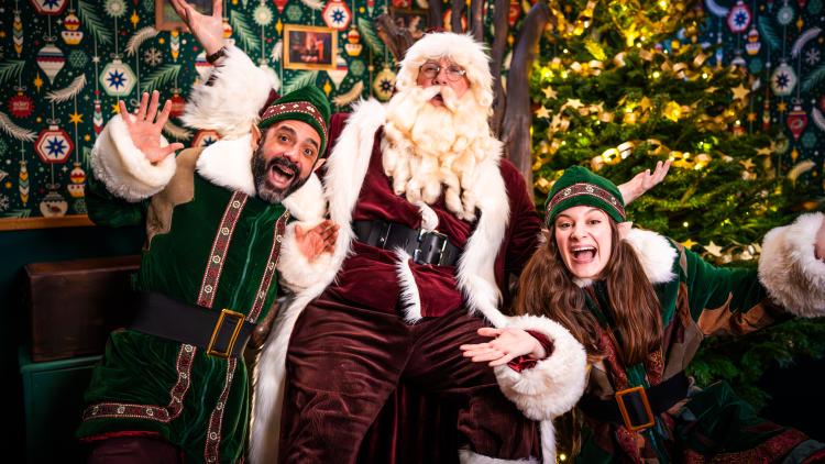 Father Christmas in a red suit and white beard with his playful Elves smiling at the camera