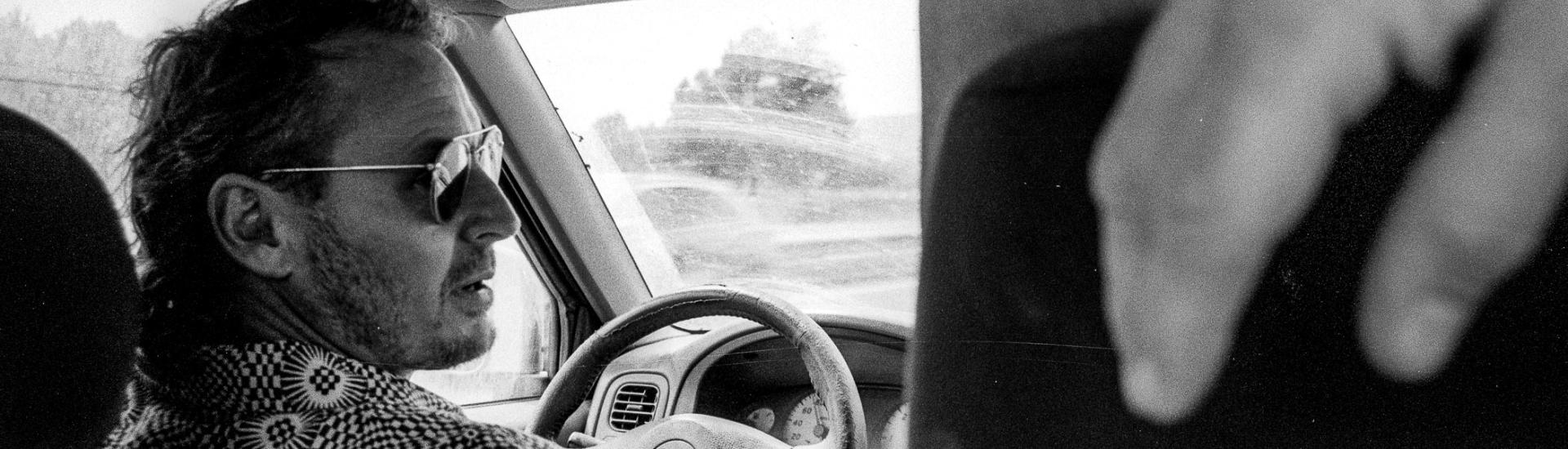 Black and white photo of Ben Howard driving a car taken from the back seat